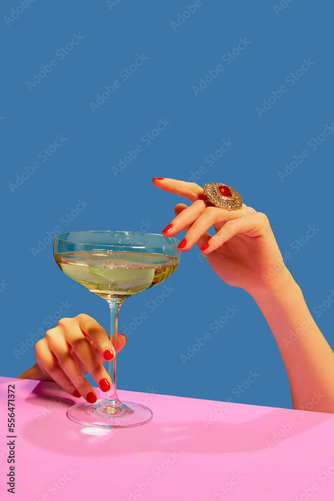 Female hands holding glass with champagne over blue pink background. Festive celebration. Food pop art - obrazy, fototapety, plakaty 