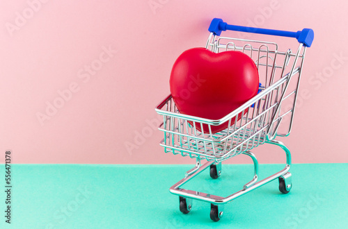 Shopping trolley with red heart on pink and mint background. Concept shopping and sale gifts for Valentines day. Declaration of love. Red heart as a symbol of love. Copy space for our text