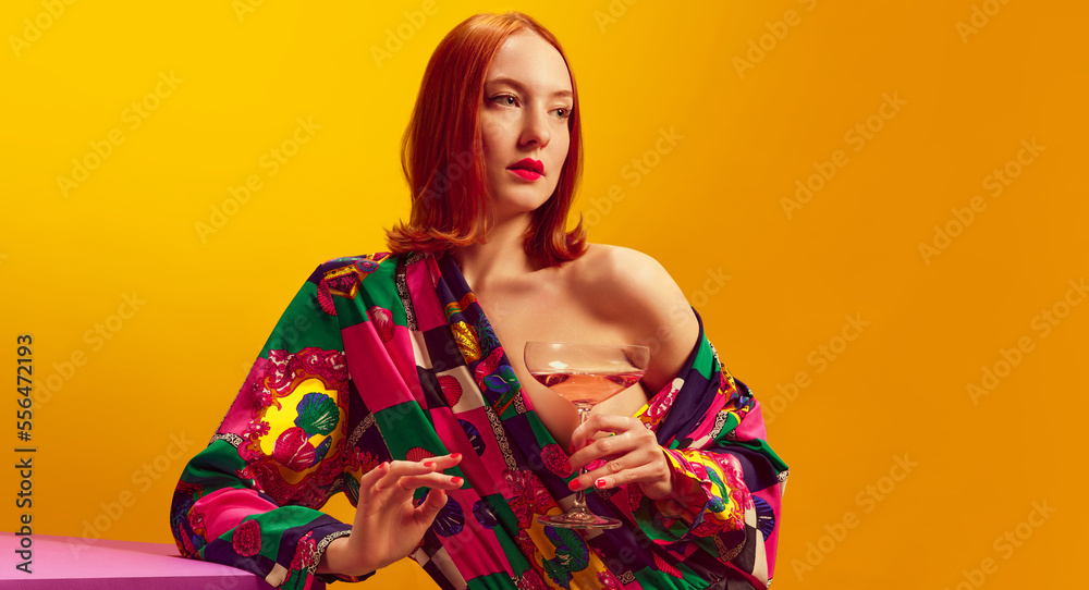 Young beautiful woman in bright costume holding champagne over yellow background. Female party. Traditional taste