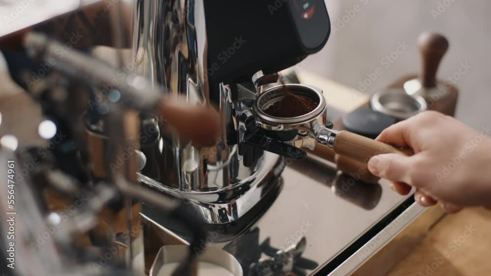 Close-up handheld shot barista inserts steel horn holder portafilter into professional coffee machine grinder. Grinding coffee beans, process of making espresso, ground coffee