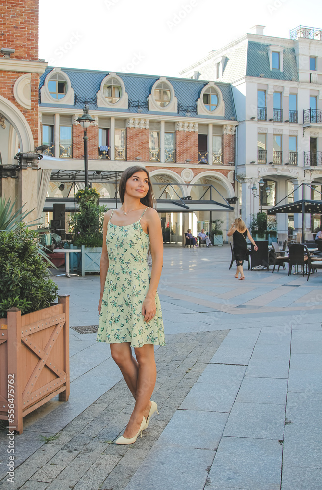 Nice brunette young woman wearing yellow dress walking in city.