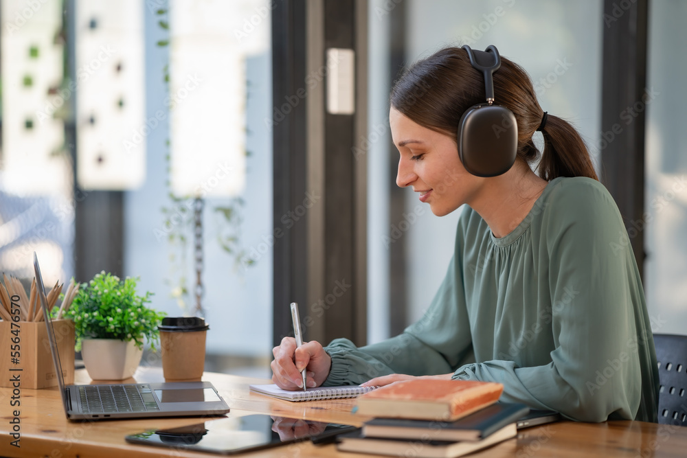 Pretty young businesswoman working on a laptop and taking notes in the office. Pretty young businesswoman working on a laptop and taking notes in the office.