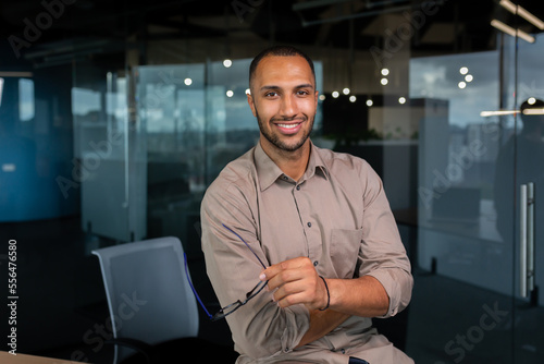Slika na platnu Portrait of african american businessman in office, man in shirt standing near window smiling and looking at camera, programmer working inside development company