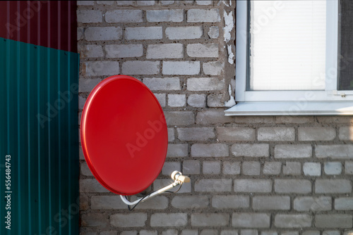 Satellite dish of red color on facadehouse.