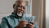 Happy african american satisfied winning bet elderly retired man counting savings mature male with pile dollars counting banknotes successful business investment profit in currency comfortable old age
