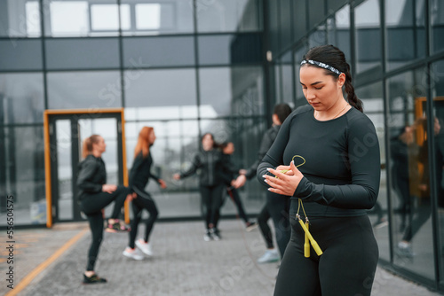 With yellow colored jump rope. Group of sportive women is outdoors near black building
