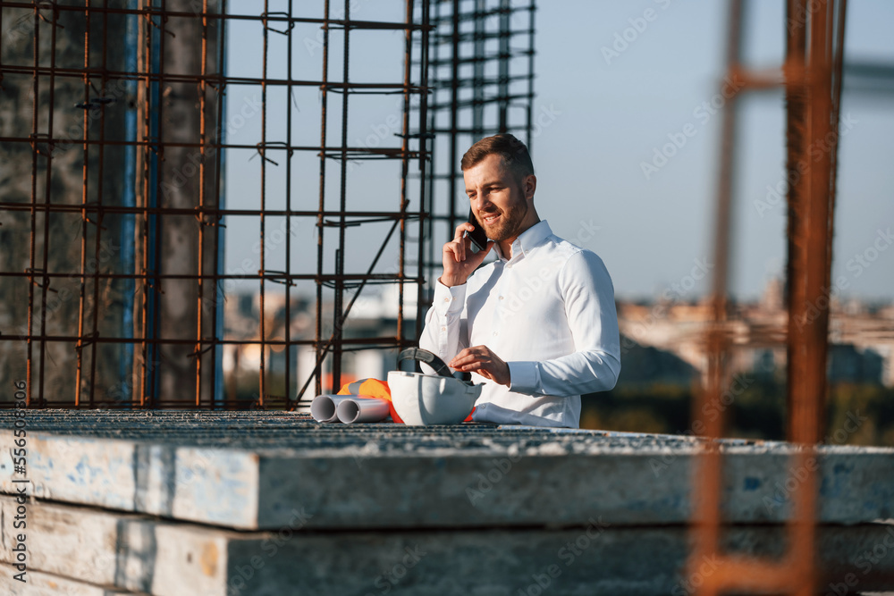 Standing and talking by phone. Businessman in formal clothes is on the construction site at daytime Standing and talking by phone. Businessman in formal clothes is on the construction site at daytime