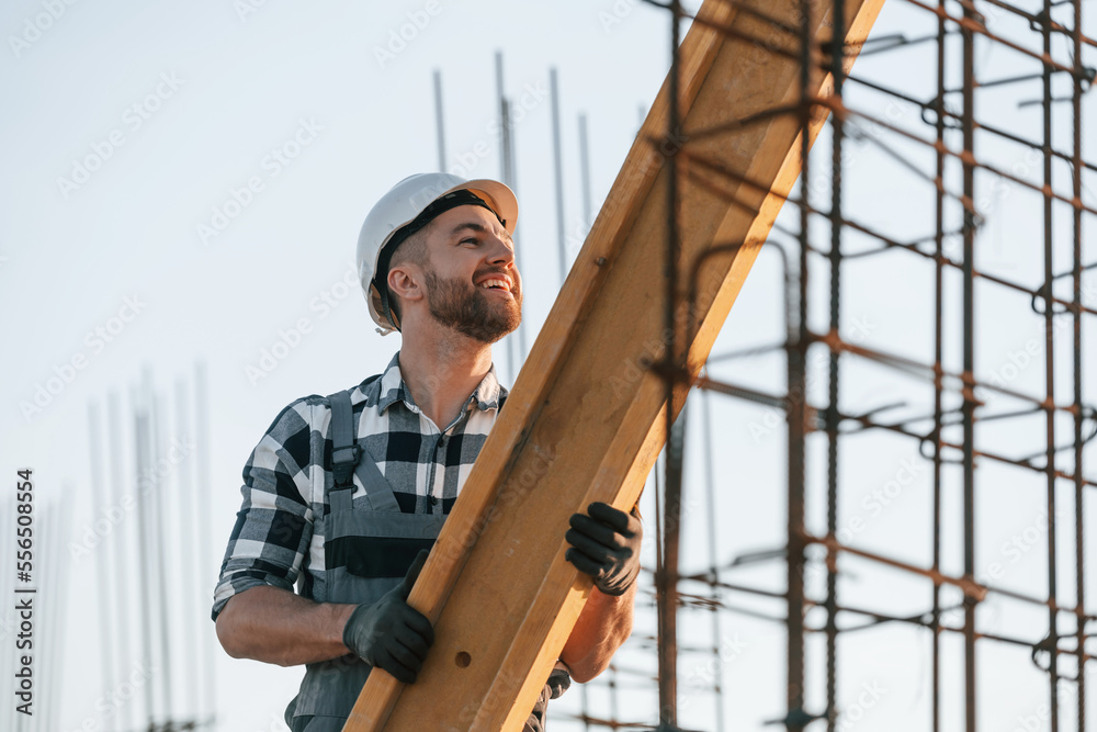 Man is working on the construction site at daytime. Moving the big wooden plank Man is working on the construction site at daytime. Moving the big wooden plank