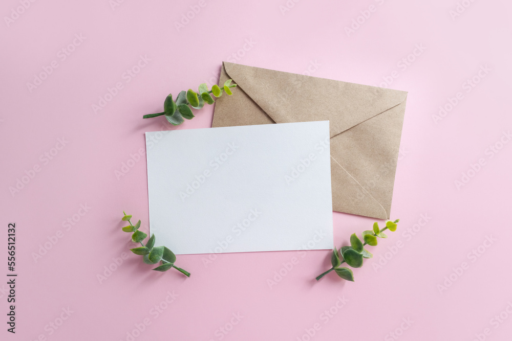 Blank sheet of paper and craft envelope on pink background surrounded by eucalyptus branches. Wedding mockup for invitation. Blank sheet of paper and craft envelope on pink background surrounded by eucalyptus branches. Wedding mockup for invitation.