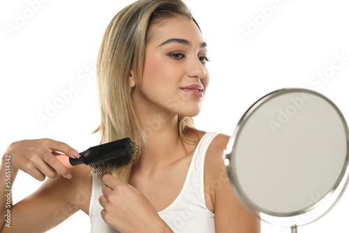 Young woman brushing healthy hair in front of a mirror on a white background