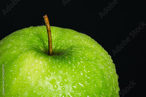 Green apple in drops of water on a black background isolated.