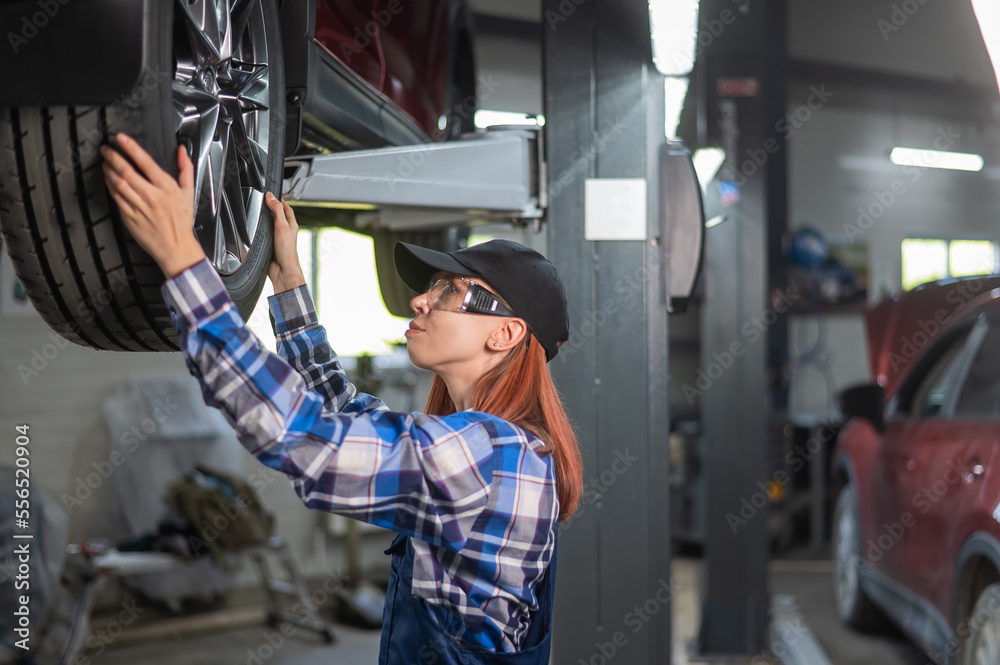 Female mechanic adjusting the tire of the car that is on the lift. A girl at a man's work. Female mechanic adjusting the tire of the car that is on the lift. A girl at a man's work.