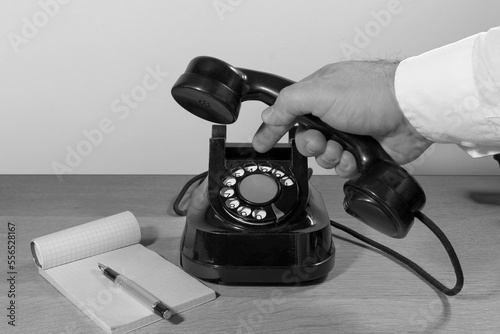 Obraz na plátně Old telephone set on a wooden table, Man's hand dialing a phone number on a phone disk