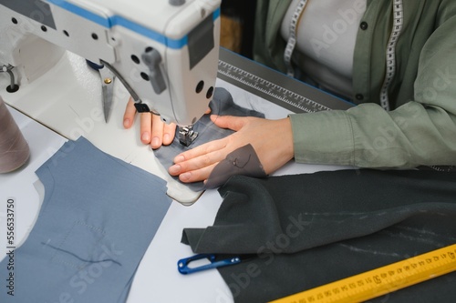 Young dressmaker woman sews clothes on working table. Smiling seamstress and her hand close up in workshop.