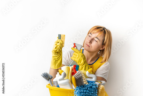 Happy young caucasian woman in a uniform wearing yellow rubber gloves and holding bucket full of cleaning supplies. Cleaning company service advertisement. Free space for text. House cleaning concept