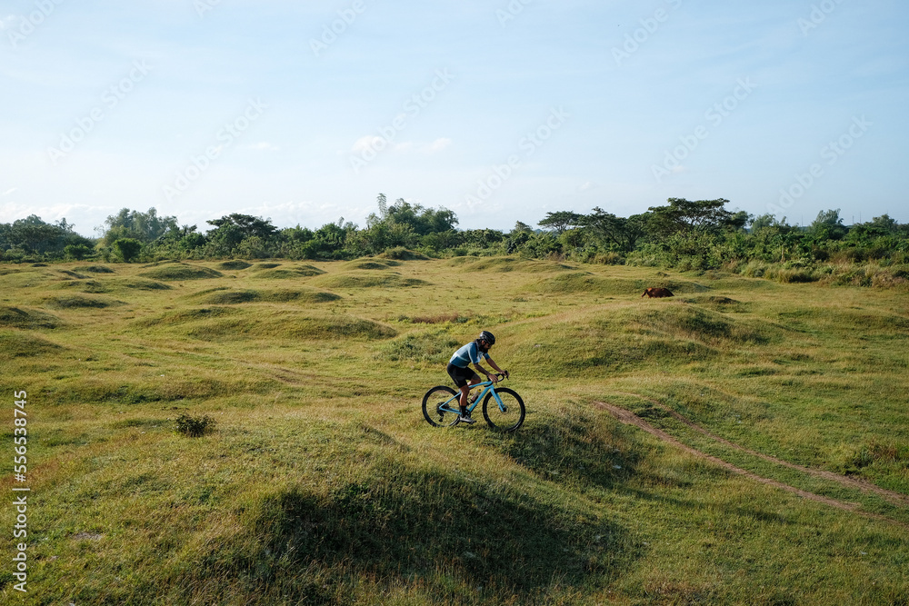 A young bearded cyclist is biking through a field