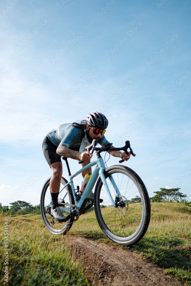 A young bearded cyclist is biking through a field