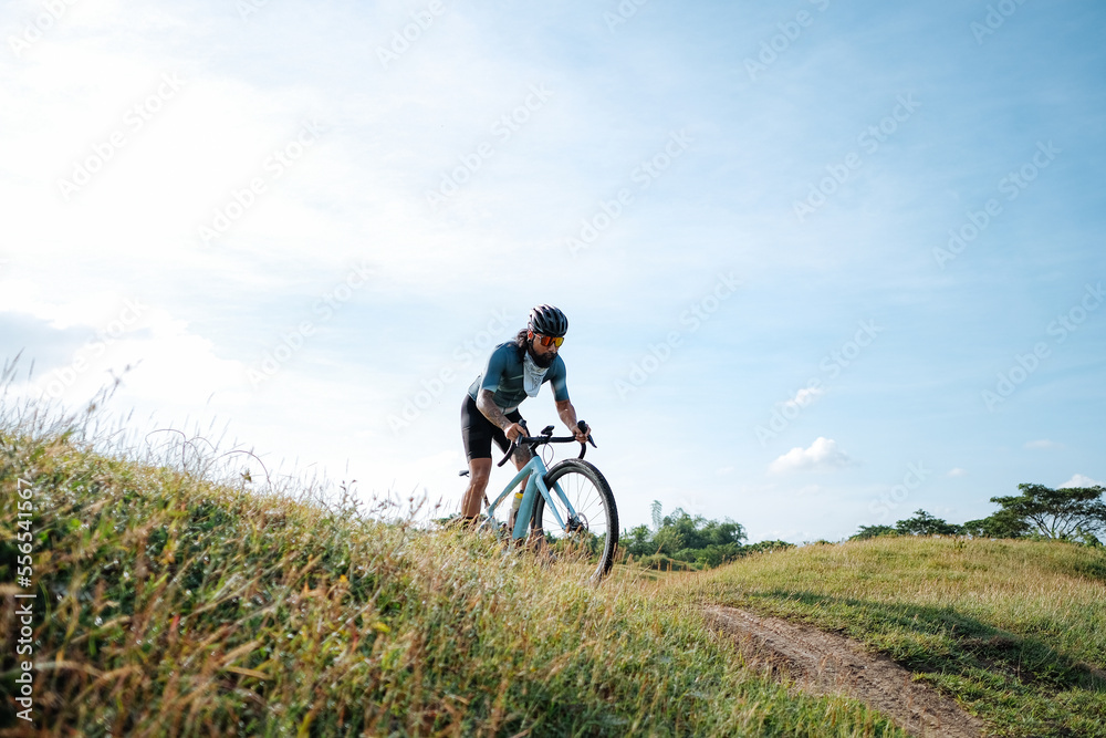 A young bearded cyclist is biking through a field A young bearded cyclist is biking through a field