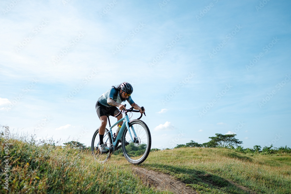 A young bearded cyclist is biking through a field