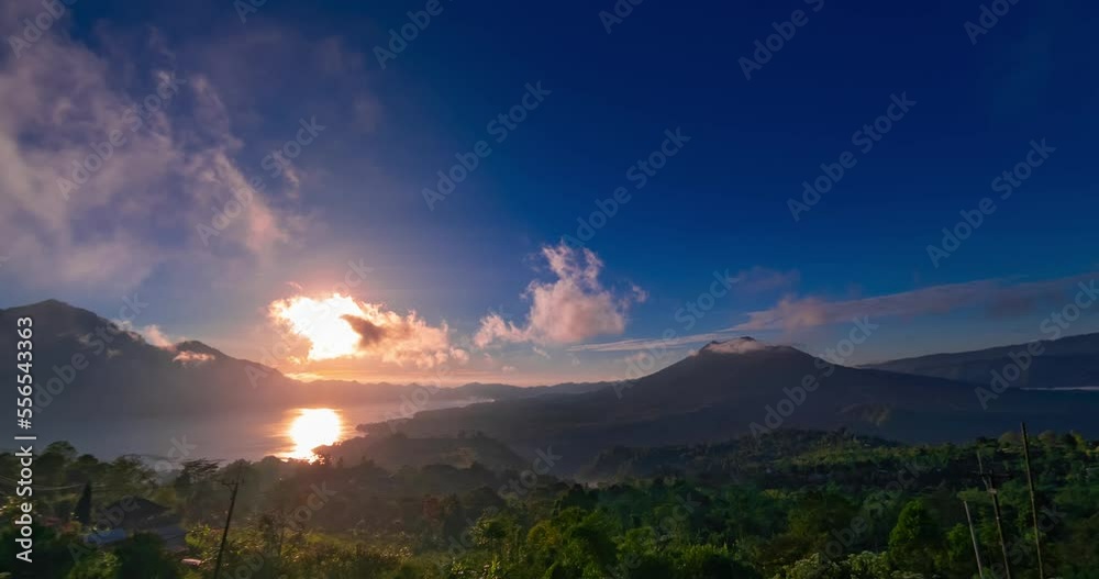 Sunset hyperlapse with view on volcanoes and lake on Bali. Clouds are moving fast in blue sky, the sun is setting