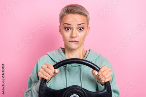 Photo portrait of pretty young girl nervous bite lips hold steering wheel dressed stylish khaki clothes isolated on pink color background