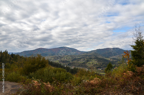 Autumn landscape with colorful trees, village on a hillside in a valley and mountains. Ukrainian Carpathians in the fall