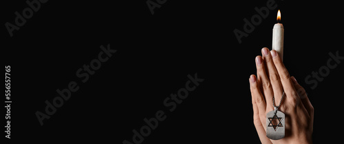 Hands of Jewish woman with burning candle and dog tag honoring victims of Holocaust on dark background with space for text photo