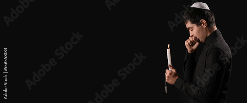 Praying Jewish man with burning candle on dark background with space for text. International Holocaust Remembrance Day photo