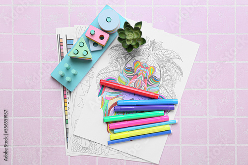 Coloring pages, felt-tip pens, educational blocks and flowerpot on pink tile background