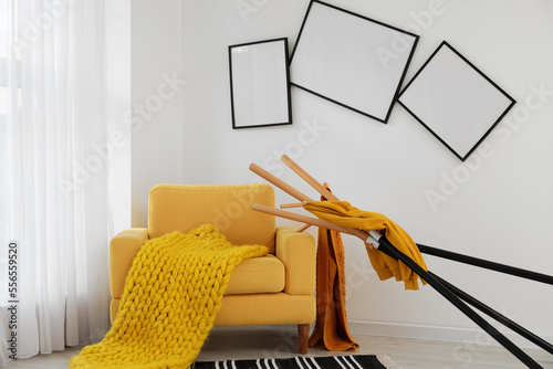 Εκτύπωση καμβά Interior of messy living room with yellow armchair, clothes stand and crooked fr