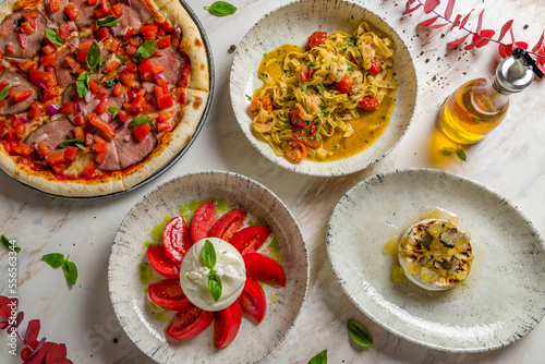 Salad with buratta cheese and tomatoes on bowl, pizza with roastbeef and tomatoes, fried camambert with truffle and pasta tagliatelli with shrimps on marble table top view