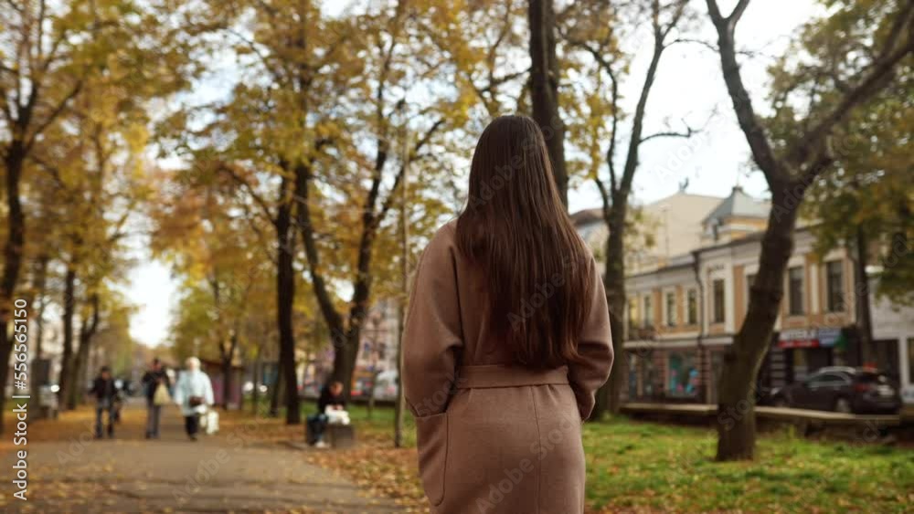 Young woman in an autumn coat walks along an alley Young woman in an autumn coat walks along an alley