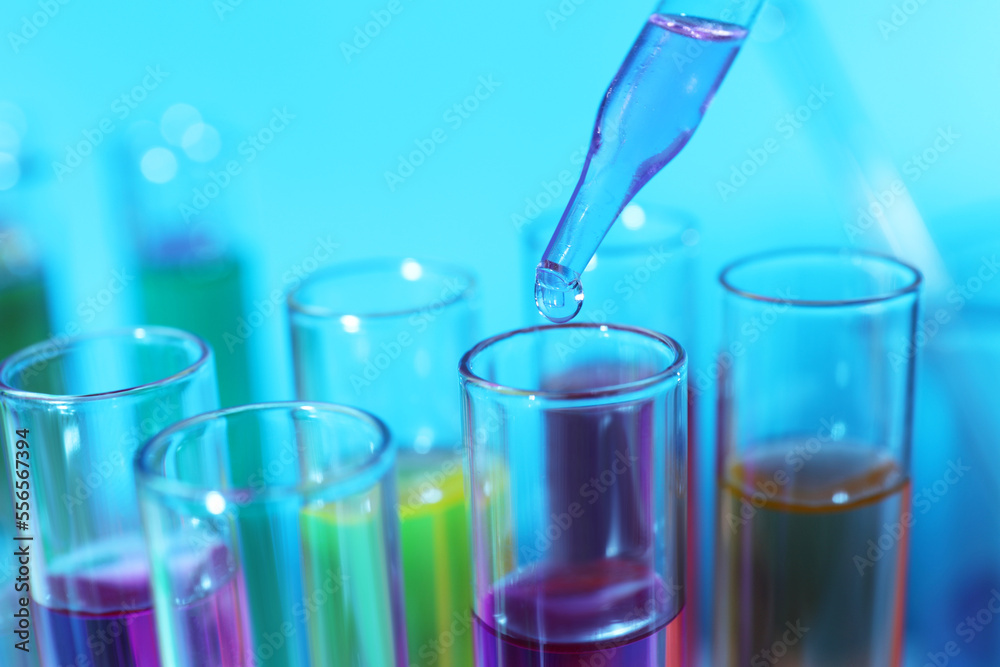 Dripping liquid from pipette into test tube on light blue background, closeup Dripping liquid from pipette into test tube on light blue background, closeup