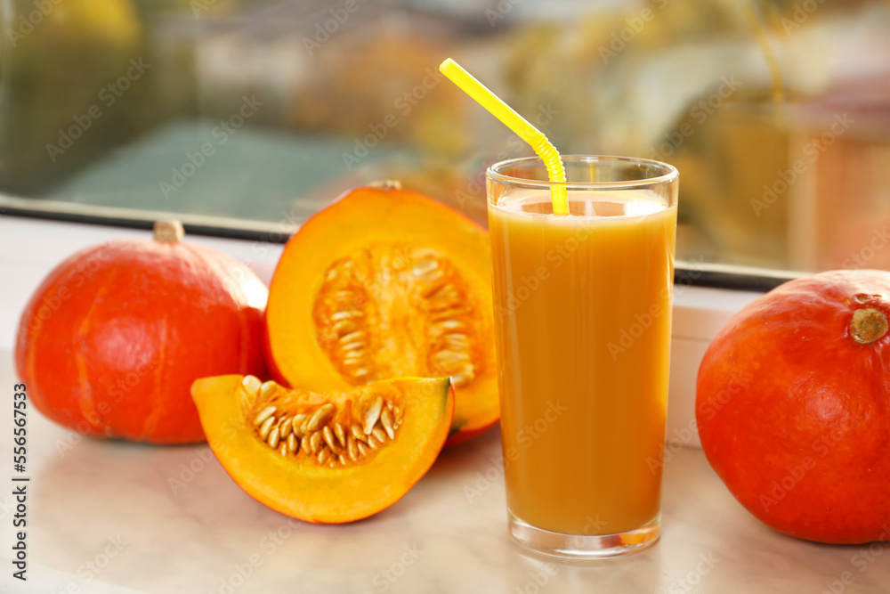Fototapeta premium Tasty pumpkin juice in glass, whole and cut pumpkins on windowsill indoors