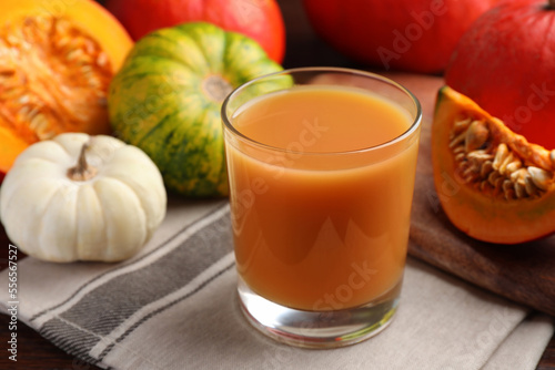 Tasty pumpkin juice in glass and different pumpkins on wooden table