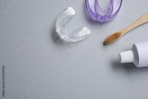 Bite correction. Toothpaste, brush and dental mouth guards on grey background, flat lay. Space for text