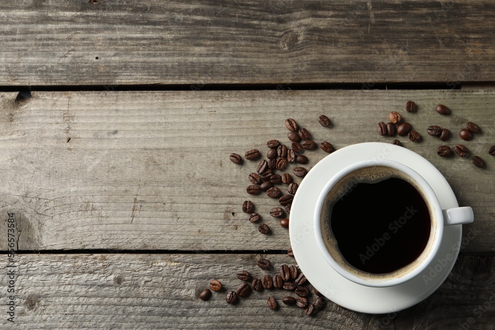 Cup of hot aromatic coffee and roasted beans on wooden table, flat lay. Space for text Cup of hot aromatic coffee and roasted beans on wooden table, flat lay. Space for text