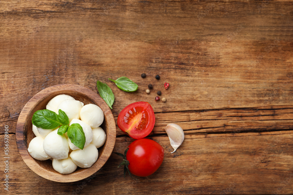 Delicious mozzarella balls in bowl, tomatoes and basil leaves on wooden table, flat lay. Space for text Delicious mozzarella balls in bowl, tomatoes and basil leaves on wooden table, flat lay. Space for text