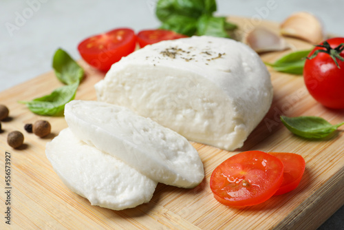 Delicious mozzarella with tomatoes and basil leaves on wooden board, closeup