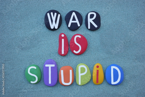 War is stupid, creative slogan composed with multi colored stone letters over green sand