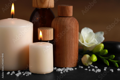 Beautiful spa composition with different care products and burning candles on black table  closeup