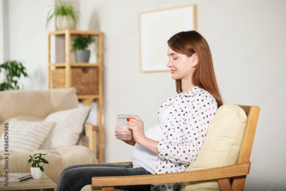 Beautiful pregnant woman holding pill and glass of water at home Beautiful pregnant woman holding pill and glass of water at home