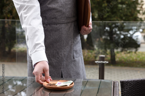 Waiter taking tips from wooden table in outdoor cafe, closeup