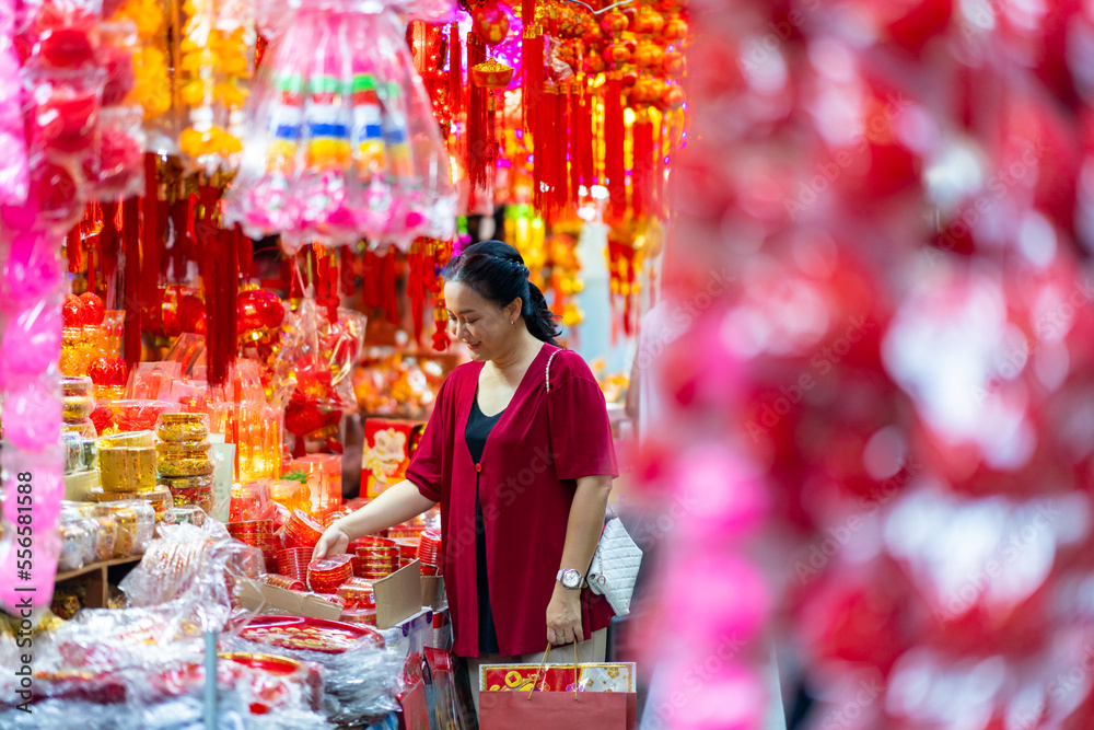 Happy Asian mature woman choosing and buying home decorative ornaments and joss paper for celebrating Chinese Lunar New Year festive at china town traditional street market. Chinese culture concept.