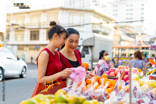 Happy Asian family mother and daughter choosing and buying fresh fruit orange together at Bangkok Chinatown street market for celebrating Chinese Lunar New Year festive. Chinese culture concept.