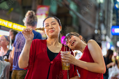 Happy Asian family on summer holiday travel vacation. Adult mother and daughter enjoy and fun outdoor city lifestyle shopping and eating street food together at Bangkok Chinatown street night market. © CandyRetriever 