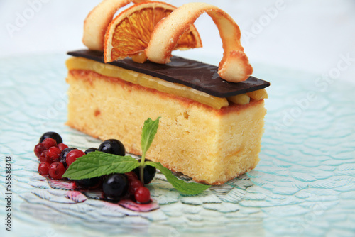 dessert sliced sponge or muffin cake with cream and chocolate sheet on top and orange cherry grapes as decoration white background. photograph on glass plate this is for restaurant menu