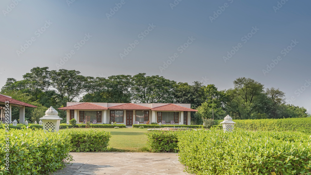 Landscape design in the park. Trimmed bushes along paved walking paths. White decorative lamps. Green grass on the lawn. Blue sky. In the distance - cottage houses. India Landscape design in the park. Trimmed bushes along paved walking paths. White decorative lamps. Green grass on the lawn. Blue sky. In the distance - cottage houses. India