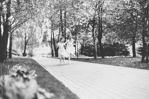 two little girls are running merrily along the path of the city park. black and white photo