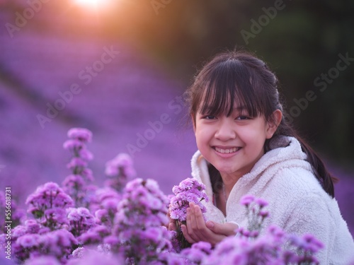 A brightly smiling little girl in white coat stands in a field of margarets flowers